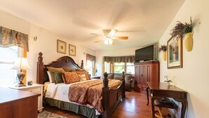 Une chambre à coucher avec un lit en bois, un bureau et une chaise. On y trouve un ventilateur de plafond et une fenêtre avec des rideaux.