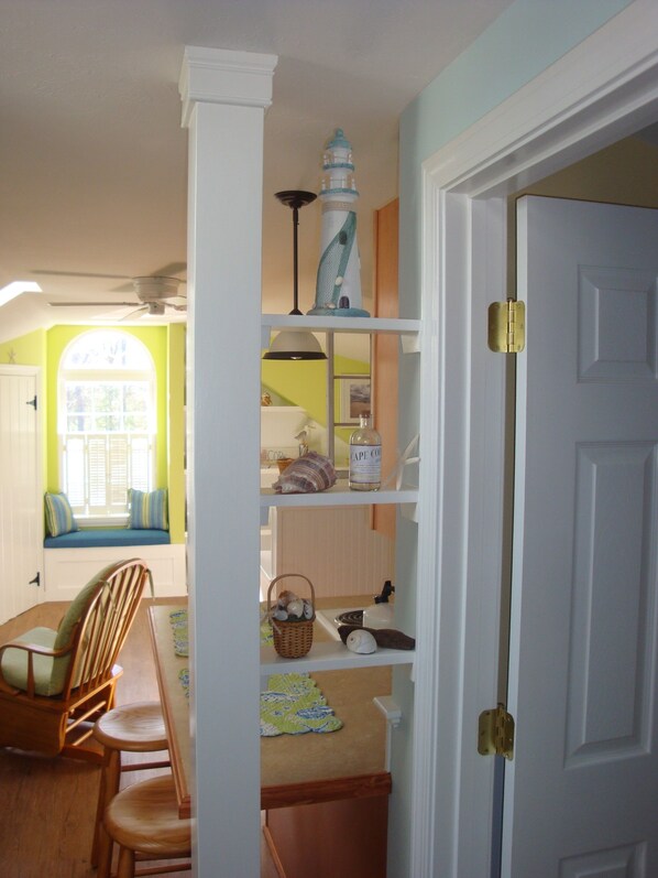 A room with a dining table, chairs, a shelf with decorative items, and a door.