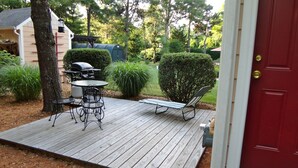 A wooden deck with outdoor furniture, a red door, and a garden with various plants. - Quaint Studio near Mashpee Commons (East Falmouth)