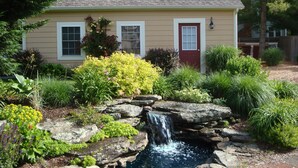 A house with a small waterfall feature in the garden, surrounded by various plants and flowers. - Quaint Studio near Mashpee Commons (East Falmouth)