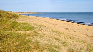 A beach with sand and grass, a wooden structure in the distance, and the ocean. - Quaint Studio near Mashpee Commons (East Falmouth)