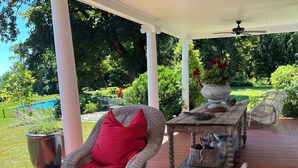 En overdækket terrasse med fletningsmøbler, et bord og en loftsvifte.