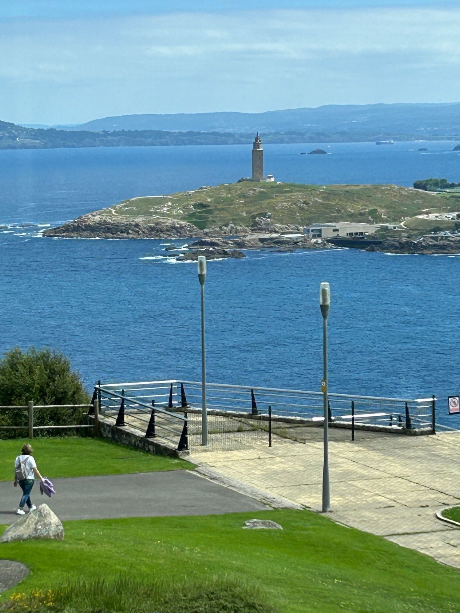 A coastal view with a lighthouse, a paved walkway, and a grassy area.