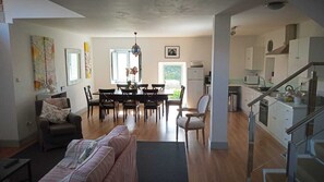 Ett rymligt vardagsrum med en soffa, en matplats med bord och stolar, ett kök med skåp och ett kylskåp samt en trappa som leder till ett annat plan.