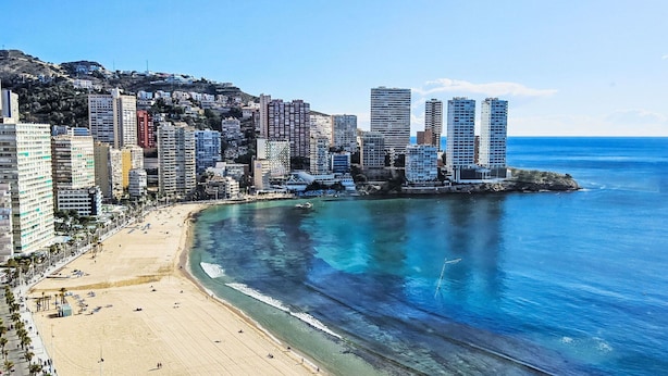 A coastal cityscape with a wide sandy beach, high-rise buildings, and a clear blue sea.