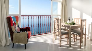 A balcony with a view of the sea, a table with chairs, and a colorful chair.