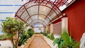 A covered walkway with tiled flooring, surrounded by potted plants and a metal railing.