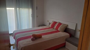 Een keurig opgemaakt bed met streepjesbeddengoed, een nachtkastje en een raam met gordijnen.