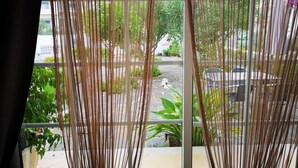 A window with vertical blinds, a view of a street with cars and greenery, and a building in the background. - Villa for rent in Nazaré Portugal (Nazaré)