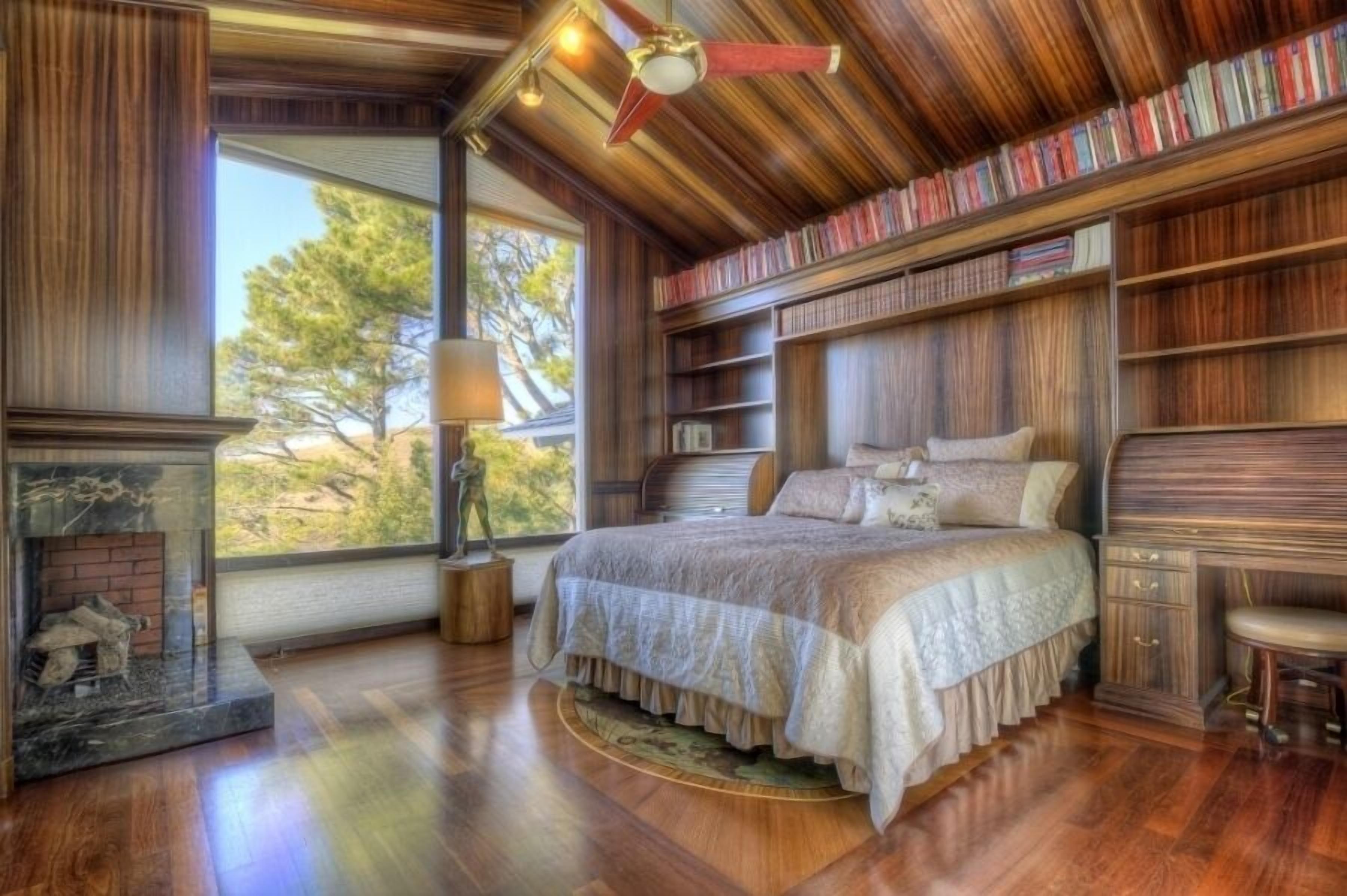 Une chambre avec un grand lit, des étagères en bois, une cheminée et une vue sur les arbres.