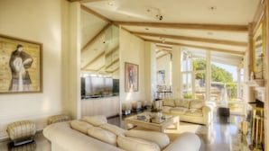 A spacious living room with a large sofa, a coffee table, and a fireplace. There is a staircase leading to another level, and a large window providing natural light. - Luxury, San Francisco Bay Area (Tiburon): 5000 sq. ft., 4 bed, 5 bath (Tiburon)