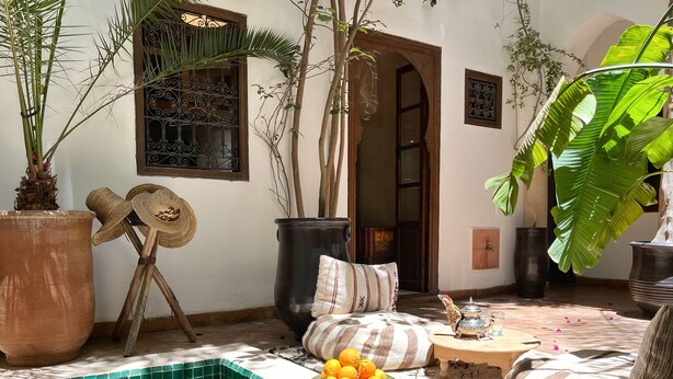 A pool area with a tiled edge, a sofa with striped cushions, and a bowl of oranges. - Gorgeous Award Winning Riad in Marrakech Medina (Marrakech)
