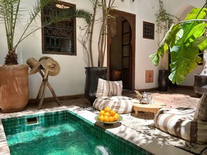 A pool area with a tiled edge, a sofa with striped cushions, and a bowl of oranges. - Gorgeous Award Winning Riad in Marrakech Medina (Marrakech)