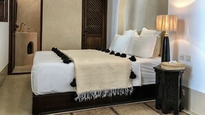 A neatly arranged bedroom with a bed, a bedside lamp, a small stool, and a wall-mounted shelf. - Gorgeous Award Winning Riad in Marrakech Medina (Marrakech)