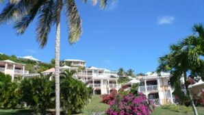 Un resort con varias edificaciones blancas, abundante follaje y plantas con flores.
