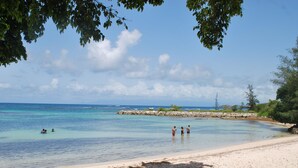 Una playa con agua turquesa cristalina, una orilla arenosa y afloramientos rocosos.