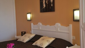 Un dormitorio con cabecera blanca, dos almohadas con estampado de árboles, un ramo de flores rosas y un cuadro en la pared.