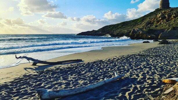 Une plage avec une grande formation rocheuse et une tour située sur une colline.
