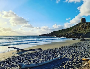 Une plage avec une grande formation rocheuse et une tour située sur une colline.
