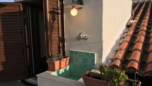 Un balcon orné de pots en terre cuite, un luminaire fixé au mur et une zone carrelée.