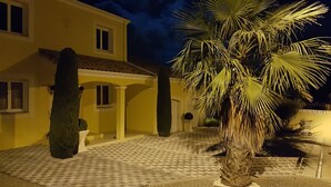 A well-lit courtyard with a palm tree, a tiled floor, and a yellow building with multiple windows.