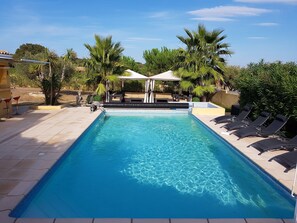 A rectangular swimming pool with clear blue water, surrounded by lounge chairs and a covered seating area. - House / Villa - Valros (Valros)