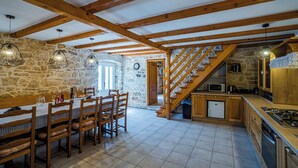 Una cocina rústica con vigas de madera, una zona de comedor con mesa y sillas, y una pared de piedra.