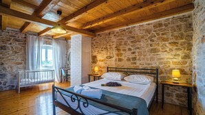 Un dormitorio acogedor con pared de piedra, vigas de madera en el techo, una cama con ropa blanca y dos lámparas de noche.