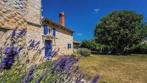 Un edificio de piedra con chimenea, contraventanas azules y un jardín de lavanda.