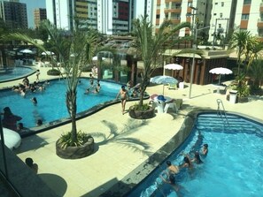 Un espace piscine comprenant plusieurs piscines, des palmiers et des espaces de détente en plein air.