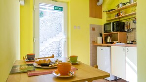A bright yellow room with a kitchen area, a dining table with breakfast items, and an exit sign on the door. - Ankora 1 with terrace and great view next to Old Town with HotTub in the garden (Dubrovnik)