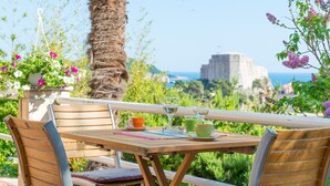 An outdoor seating area with wooden furniture, a table with a placemat, and a view of the sea and a historic building in the background. - Ankora 1 with terrace and great view next to Old Town with HotTub in the garden (Dubrovnik)