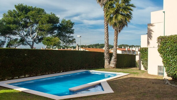 Une piscine rectangulaire dont le bord est recouvert de carreaux, entourée d’une pelouse bien entretenue et d’une haie.