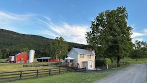 Un paysage rural avec un chemin de gravier, une grange rouge, une tour à grain blanche et une maison dotée d’un porche.