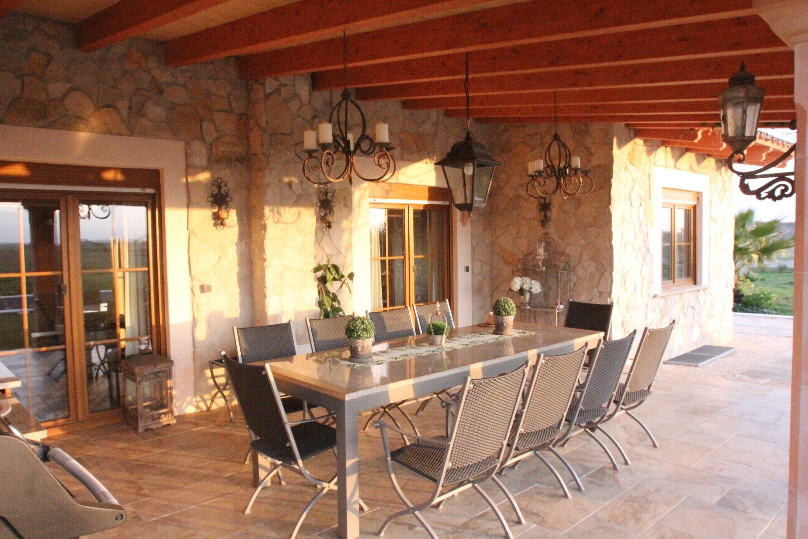 An outdoor patio with a stone wall, a wooden ceiling, and a dining table with chairs.