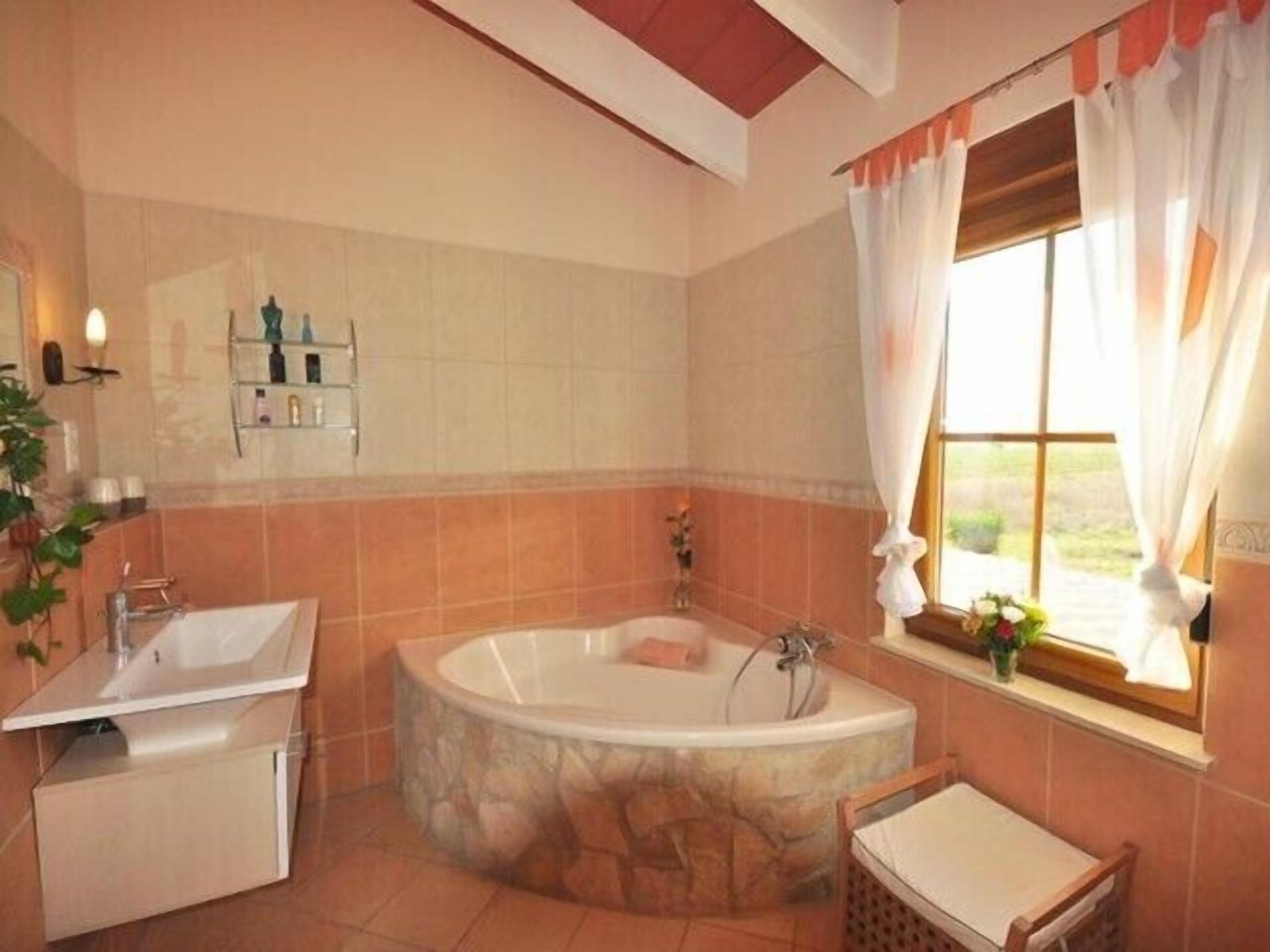 Une salle de bain avec une baignoire, deux lavabos et une fenêtre avec des rideaux.