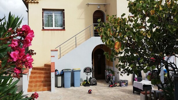 Une maison à deux étages, avec un toit recouvert de tuiles, un petit balcon et une entrée pavée de pierres.