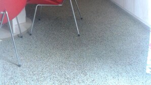 Un espace de vie compact comprenant une table à manger, des chaises rouges, un canapé, un petit coin cuisine avec un réfrigérateur et une fenêtre avec un rideau.