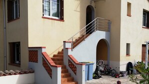 Une maison à deux étages avec un patio dallé de pierres, un escalier doté d’une rampe en métal et un panier de basketball.