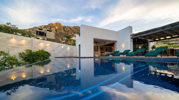 Ein Swimmingpool mit Liegestühlen, eine überdachte Terrasse und ein Bergpanorama.