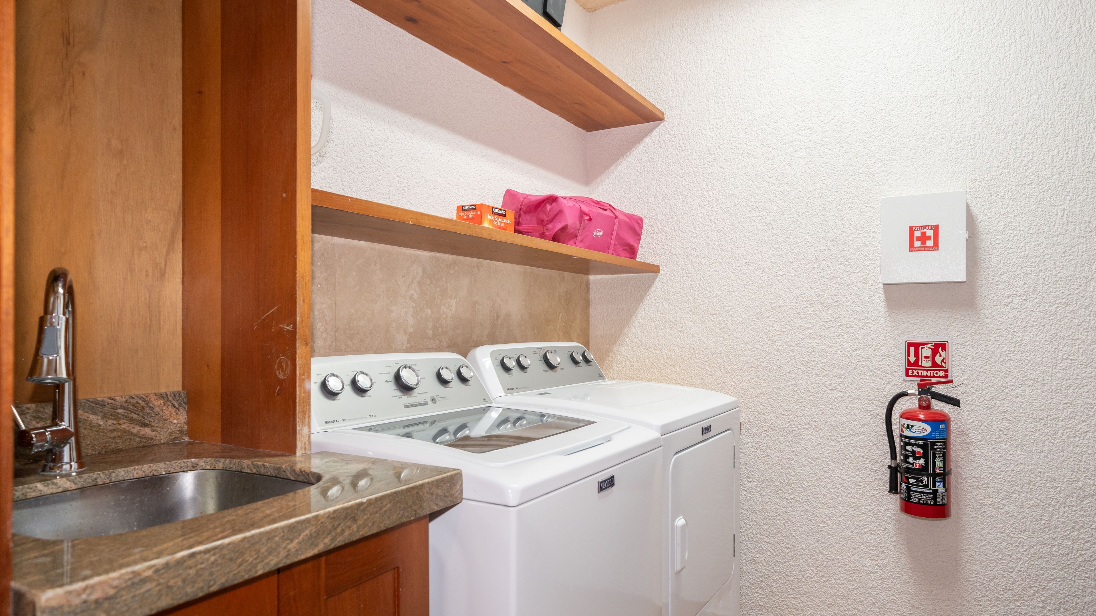 A kitchen with a stove, oven, and sink. There is a fire extinguisher mounted on the wall.