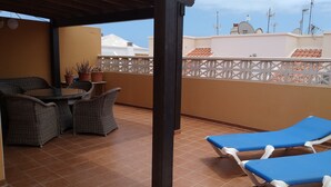 A balcony with wicker furniture, a table, and two blue lounge chairs. - An oasis in the desert of civilization (FUERTEVENTURA)