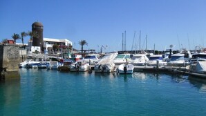 A marina with various boats docked, a prominent tower, and a building with a dome roof. - An oasis in the desert of civilization (FUERTEVENTURA)