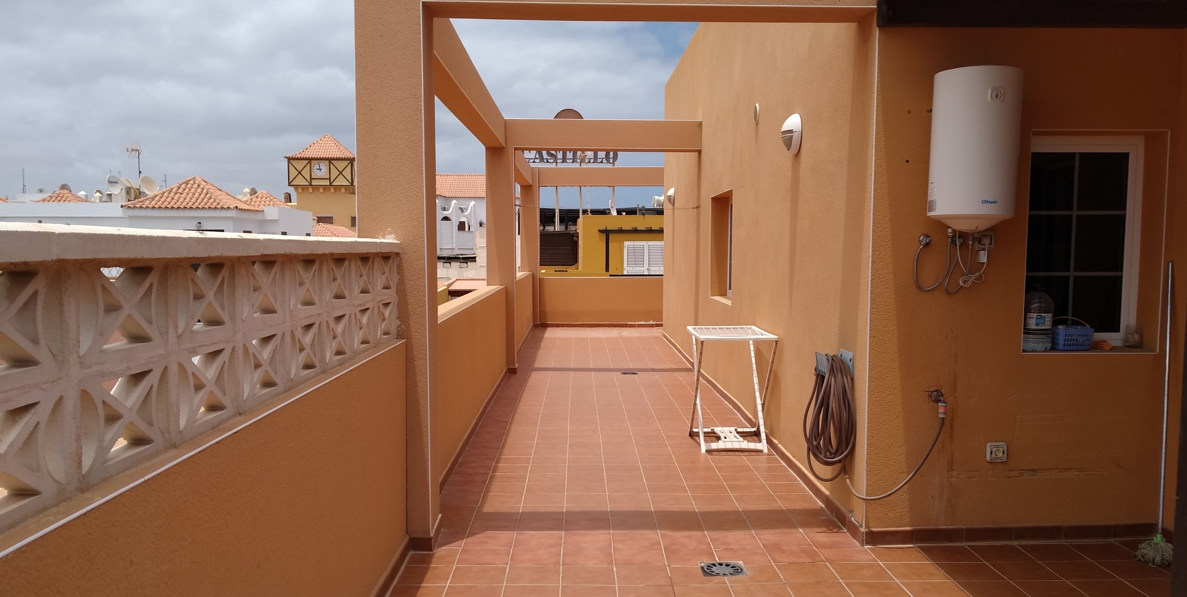 A corridor with a water heater, a small table, and a view of buildings in the background.
