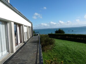 A building with large windows and a stone pathway leading to a grassy area with a view of the sea.