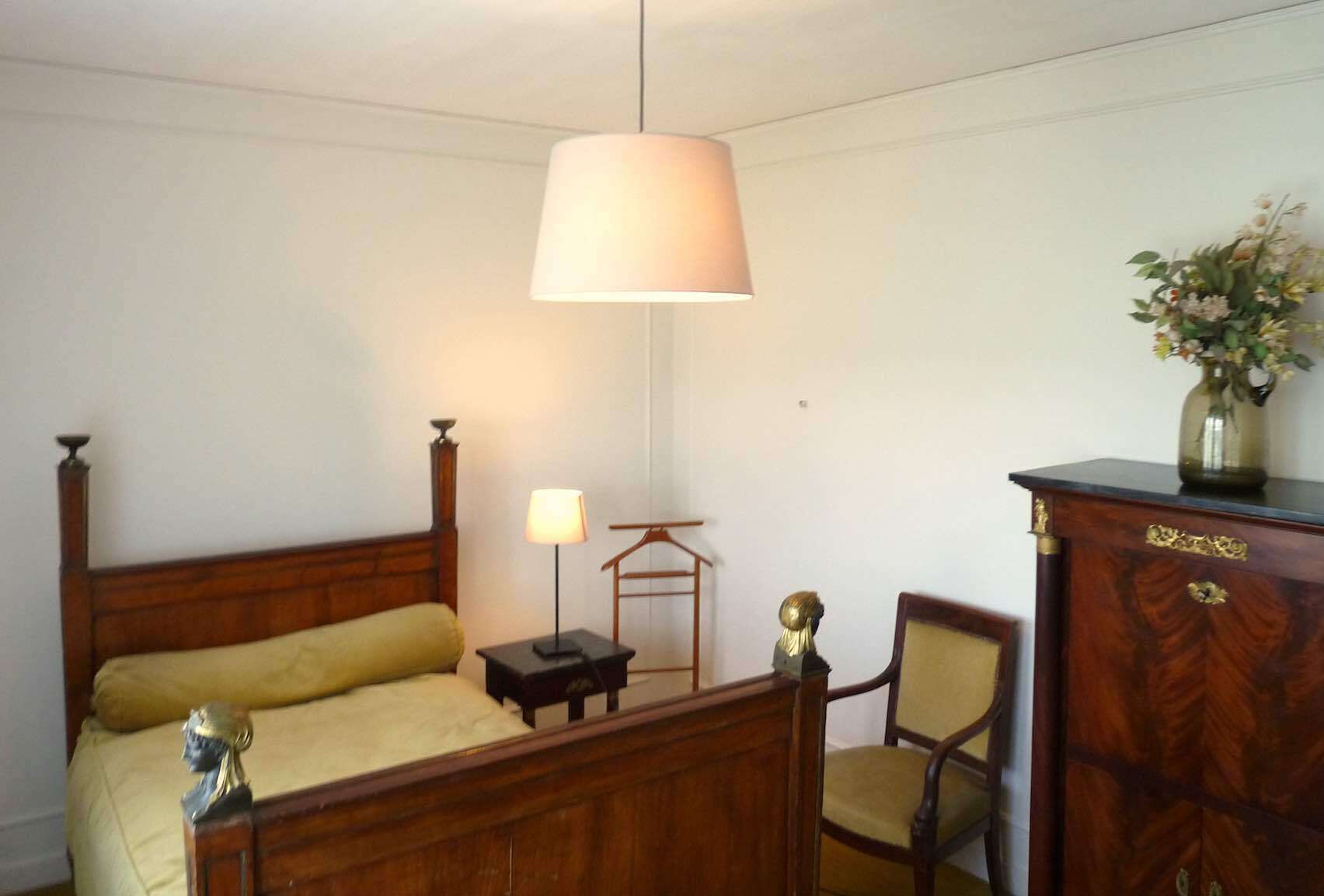 A bedroom with a wooden bed, a bedside table, a lamp, a chair, and a dresser.