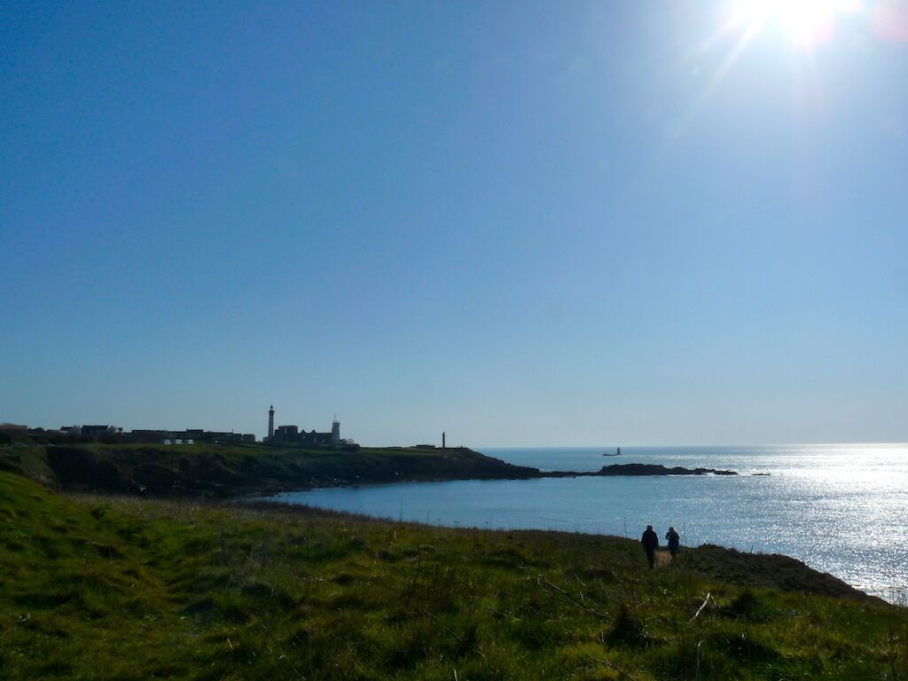 A coastal landscape with grassy terrain, a lighthouse, and a body of water.