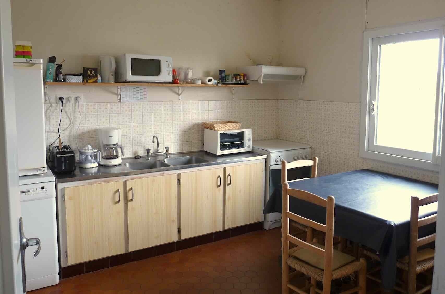 A compact kitchen with a microwave, toaster, and coffee maker on the counter, a sink, and a dining table with chairs.