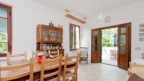 A dining area with wooden furniture, a cabinet with glass doors, and a view through an open door to an outdoor seating area.