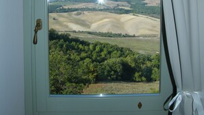 Ein Zimmer mit einem großen Fenster und Blick auf sanfte Hügel und einen klaren Himmel.